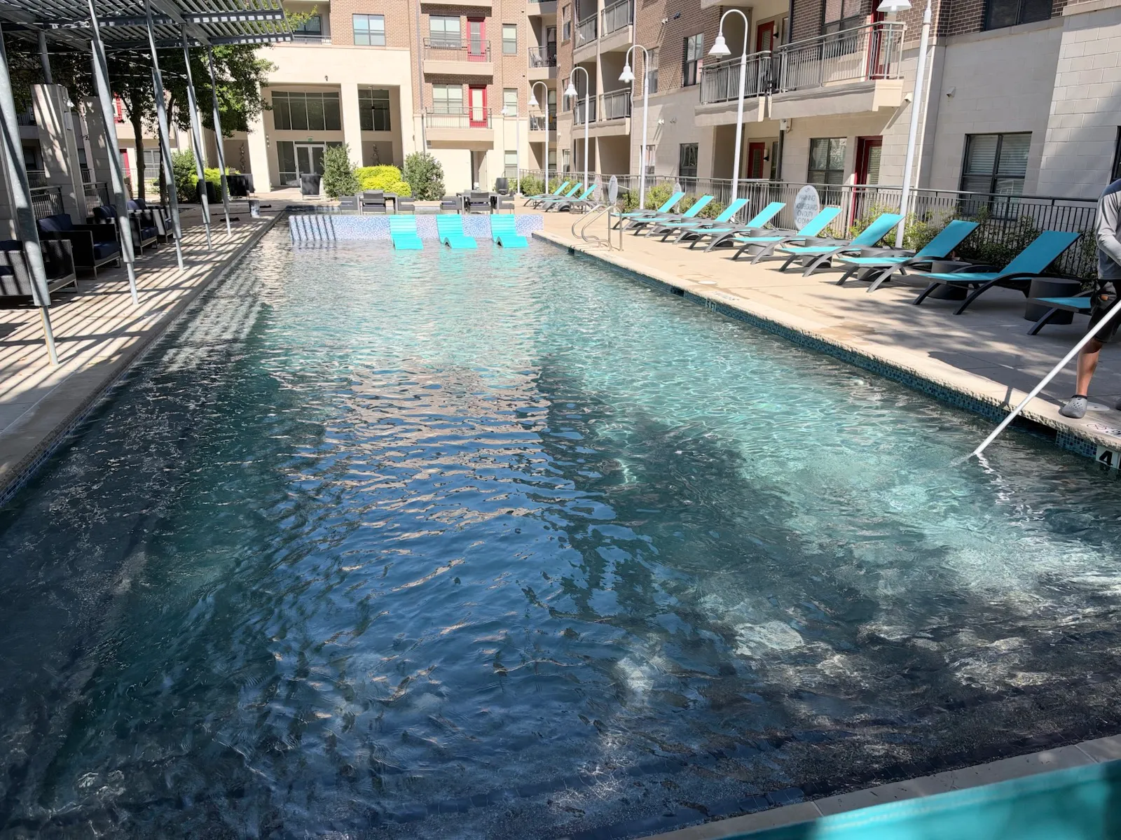 A long apartment complex pool with clear water, an in-pool tanning ledge and loungers along the deck